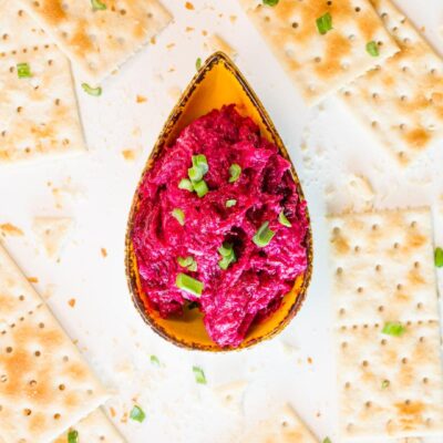 A bowl of the Ukrainian Purple Beetroot Dip with a lot of square crackers around the bowl on a big white table