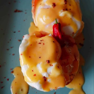 Hollandaise Sauce served over eggs with cured salmon and red chili pepper on a blue plate.