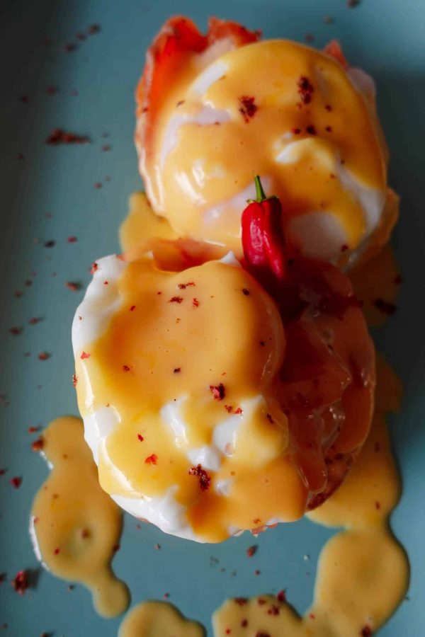 Hollandaise Sauce served over eggs with cured salmon and red chili pepper on a blue plate.