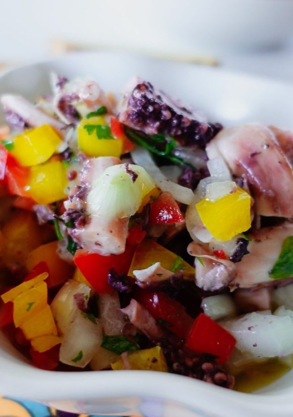 Small bowl of octopus salad on a a colorful board.
