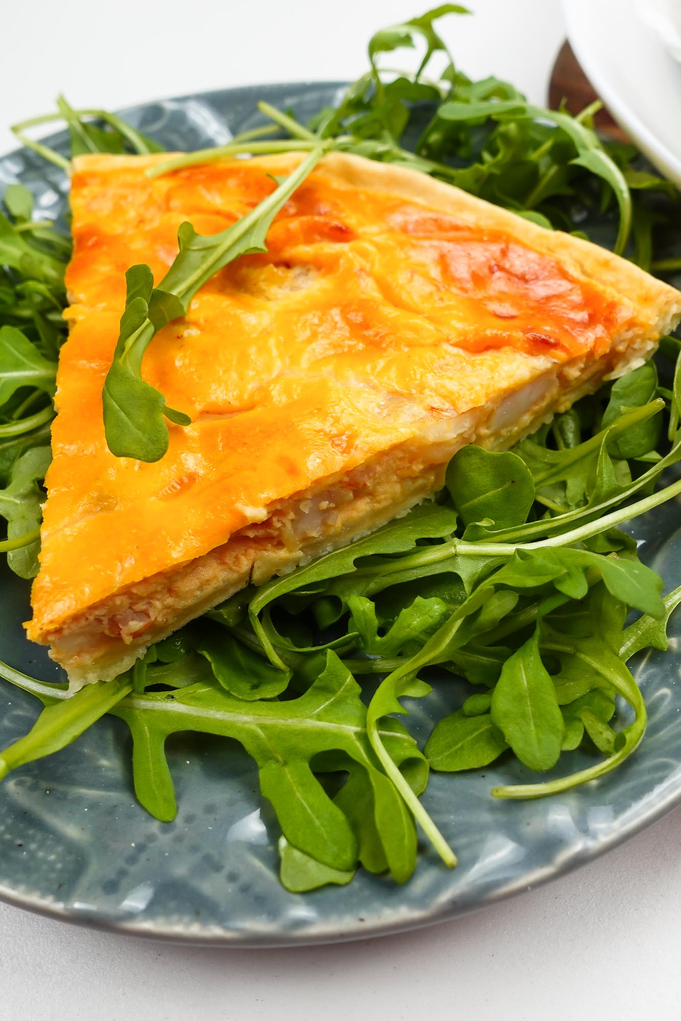 A piece of shrimp quiche on a plate with arugula.