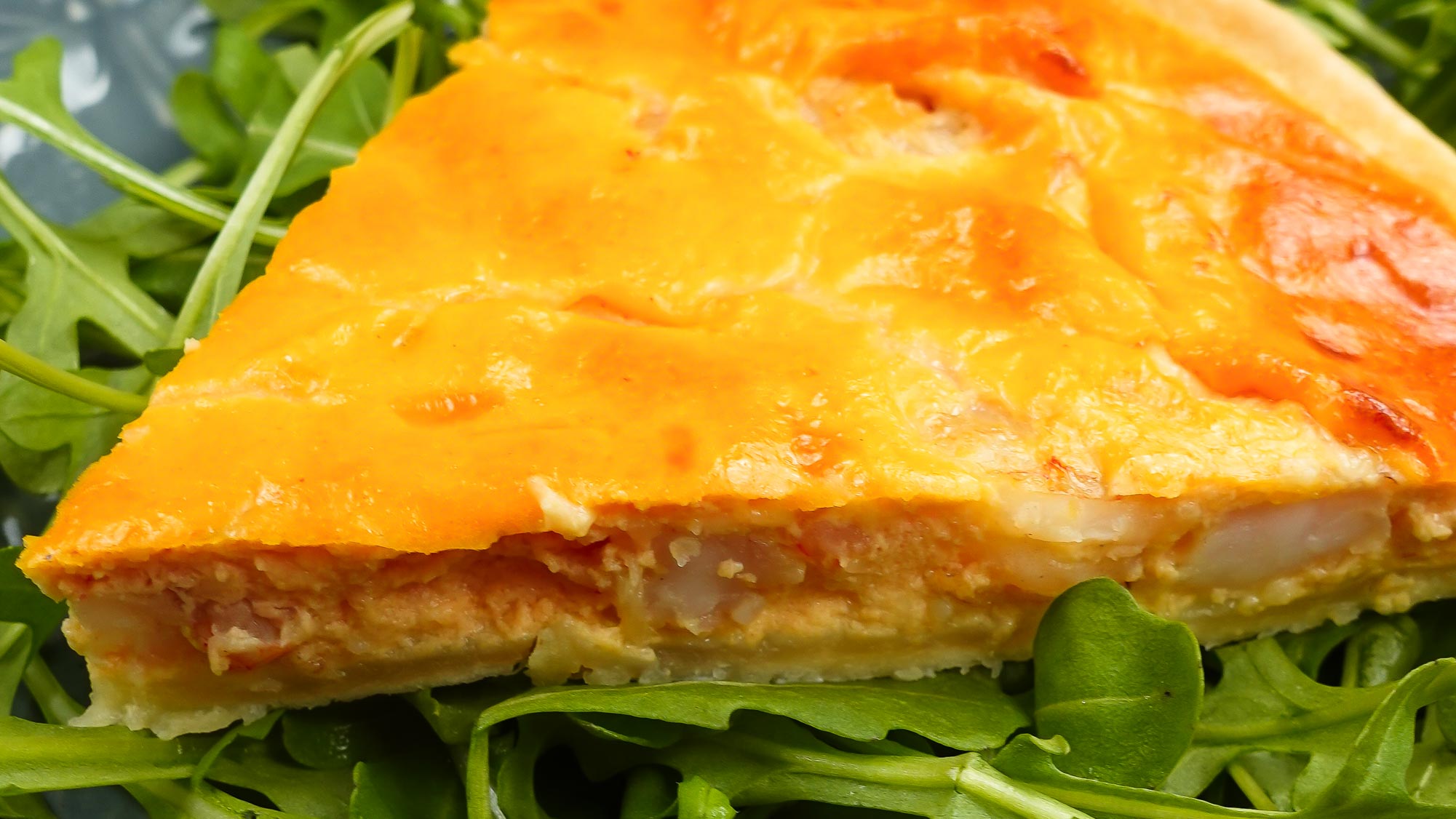 A piece of shrimp quiche on a plate with fresh arugula.
