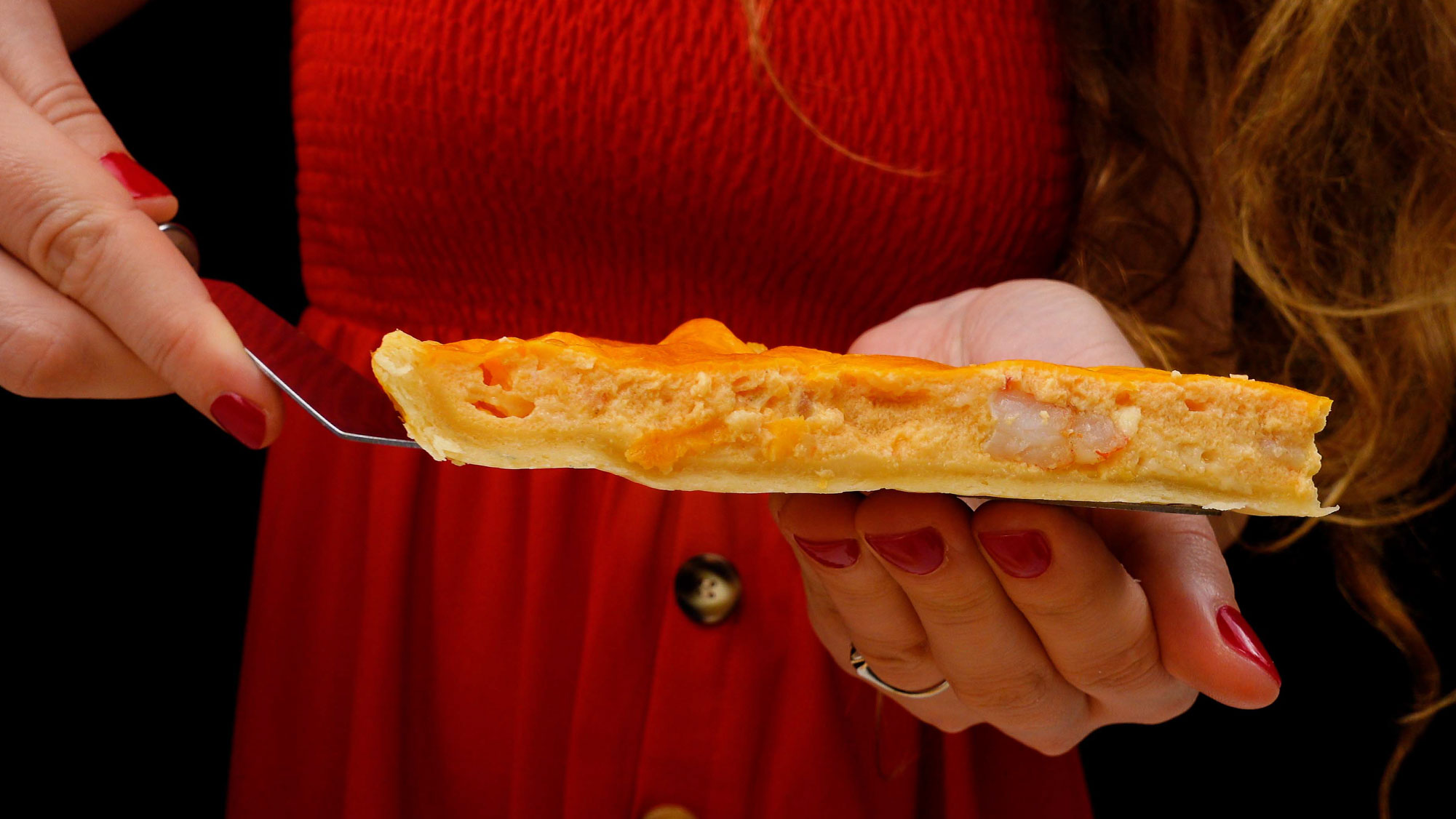 A piece of shrimp quiche in two hands. 