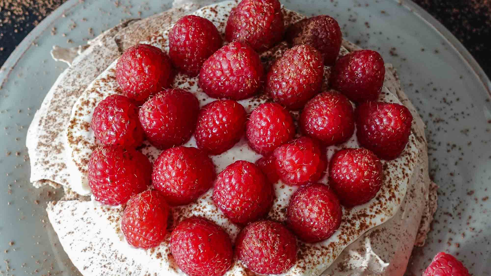 Raspberry Pavlova on a plate with fresh raspberries on a side.