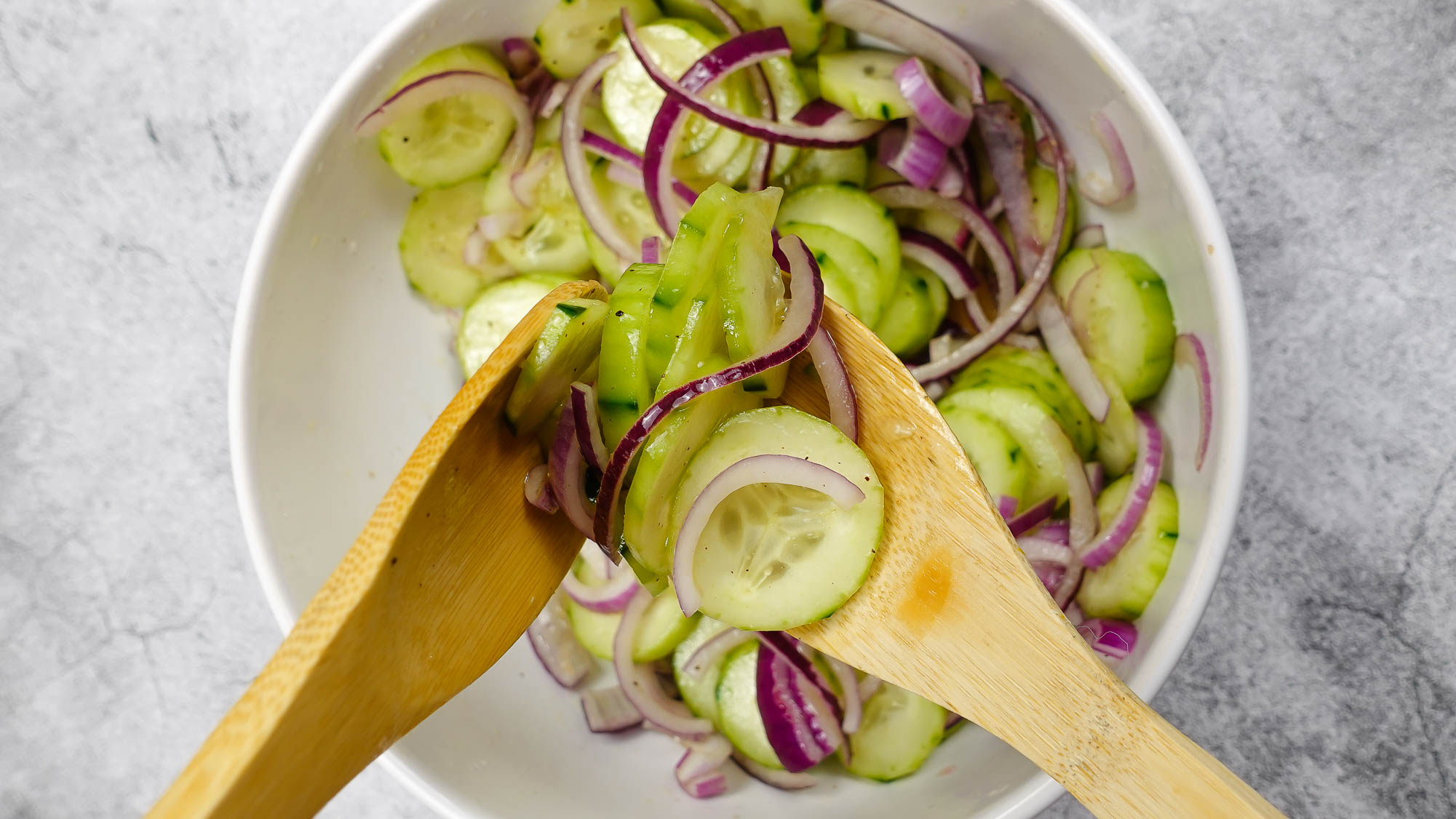 Cucumber Red Onion Salad Recipe in a big white bowl with a wooden fork and spoon.