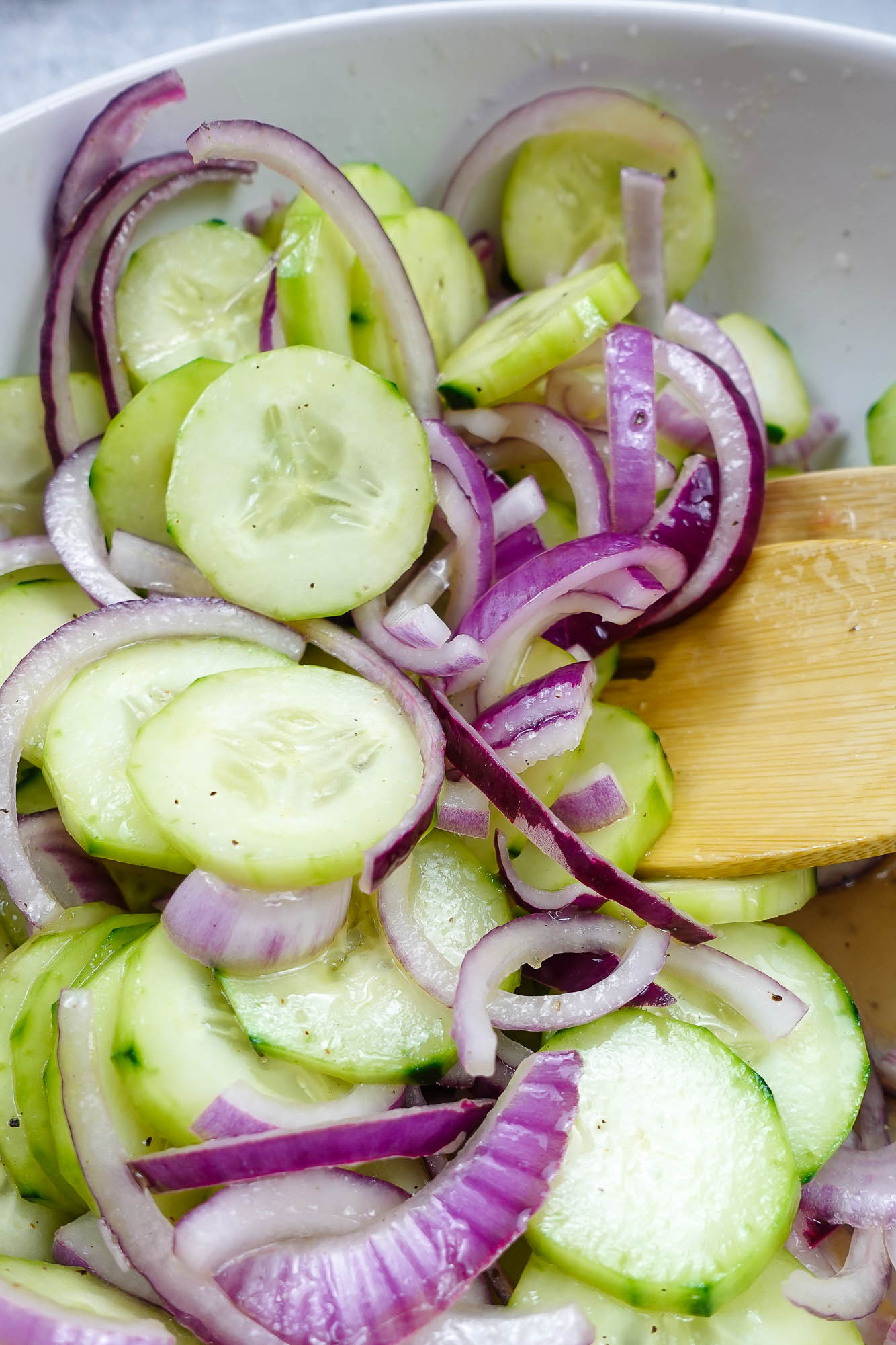 A closeup of Cucumber Red Onion Salad Recipe in a big white bowl with a spoon inside the bowl.