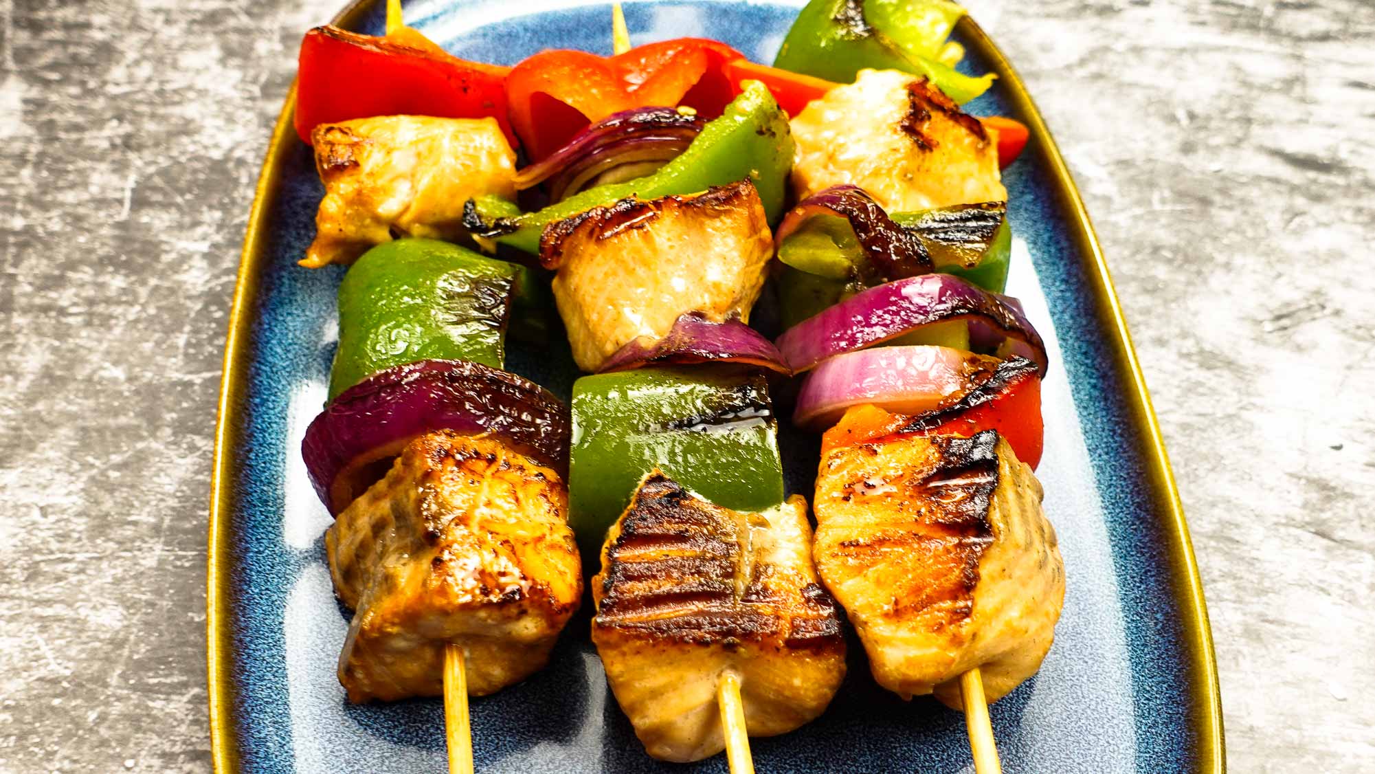 Juicy and perfectly cooked salmon kabobs on a blue plate.