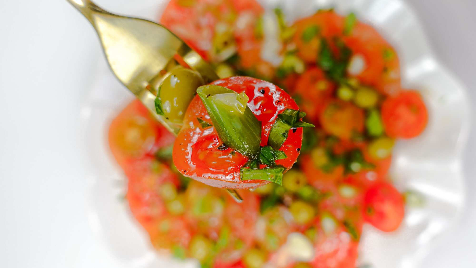 Mediterranean Tomato Salad on a plate and a fork full of salad in right hand.