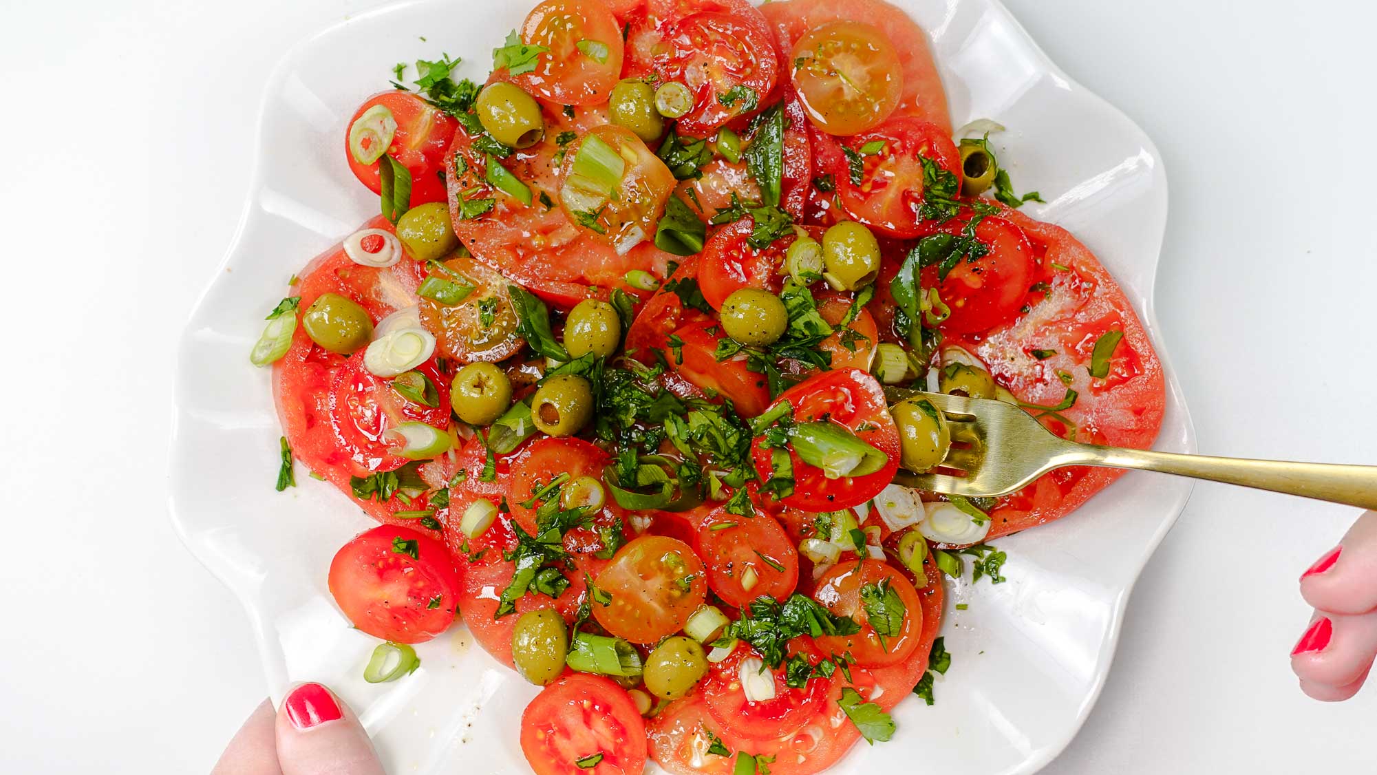 Mediterranean Tomato Salad on a plate and a fork full of salad in right hand.