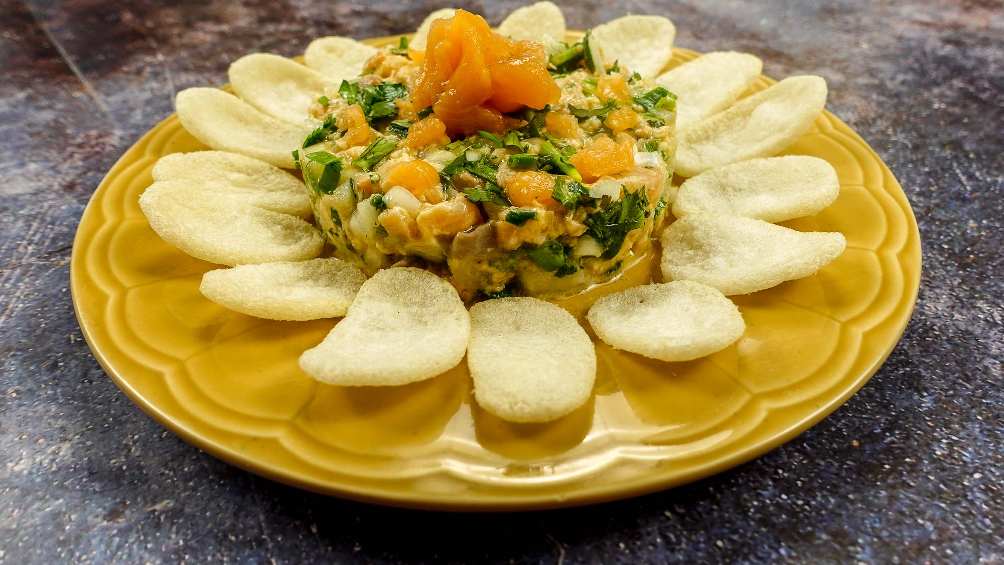 Mediterranean Salmon Tartare on a yellow plate with shrimp chips.