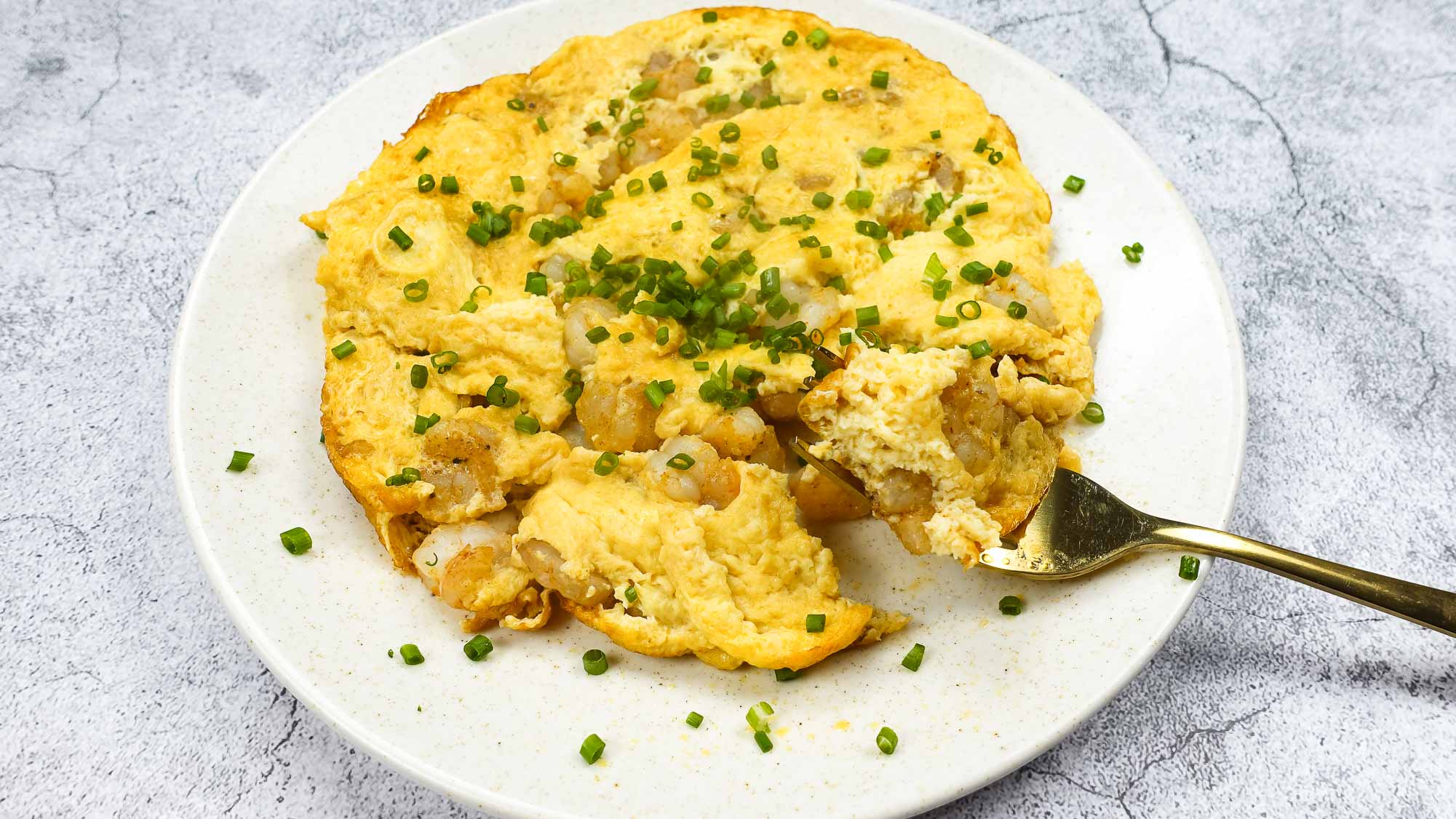 Shrimp Omelette on a plate with green onion and a fork full of omelette.