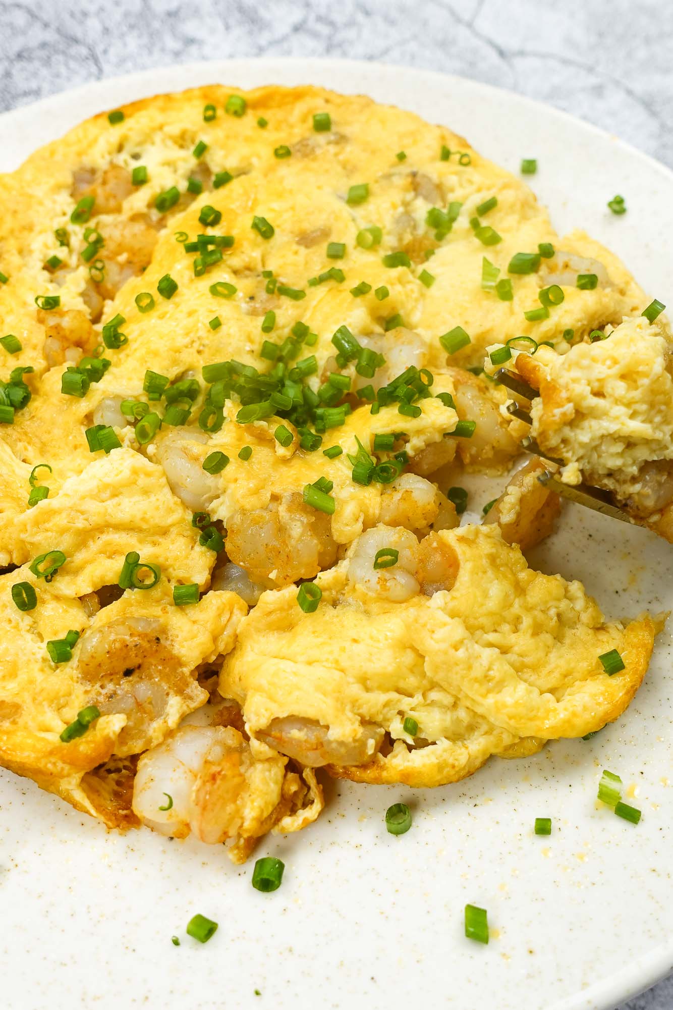 Shrimp Omelette on a plate with green onion and a fork full of omelette.