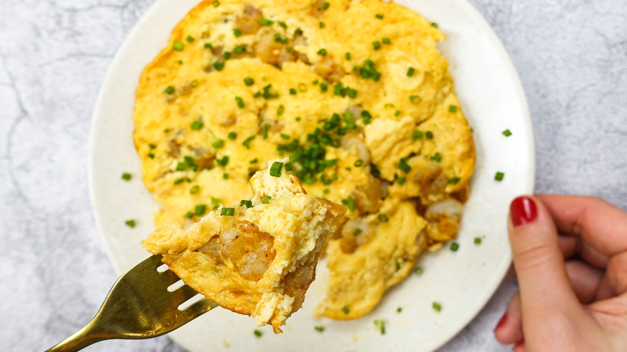 Shrimp Omelette on a plate with green onion and a fork full of omelette in one hand.
