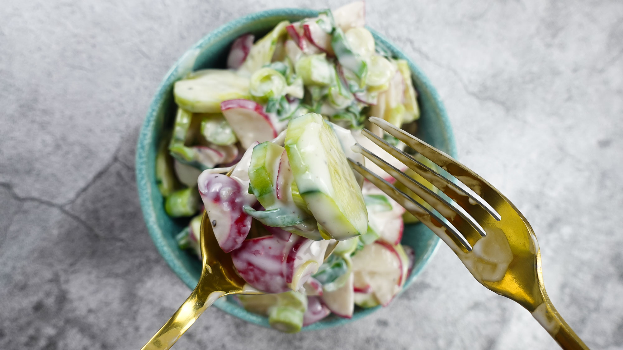 Creamy Cucumber Radish Salad in a bowl with a spoon and fork.