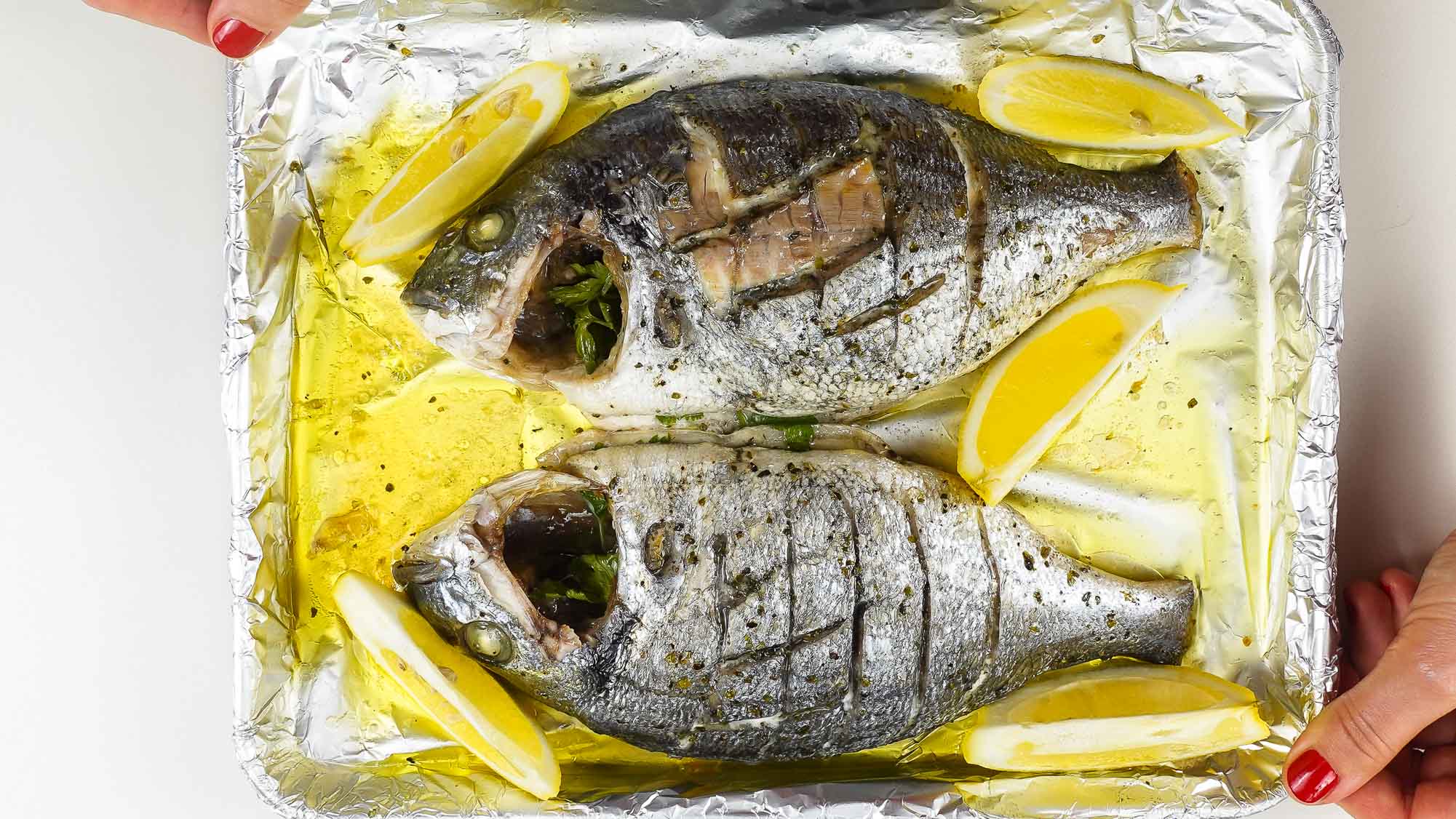 Foil baked Sea Bream with fresh lemon slices on a tray, in two hands.