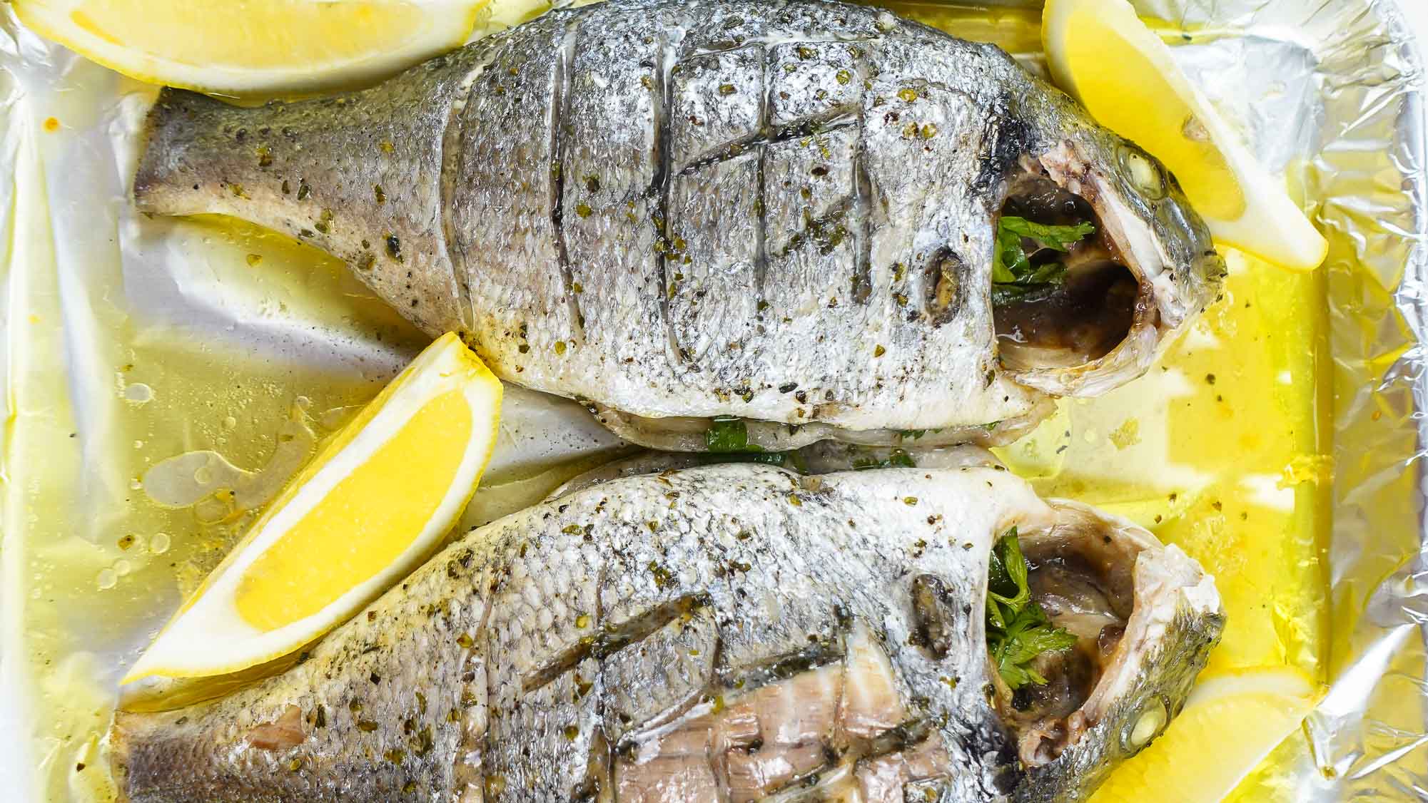 Foil baked Sea Bream with fresh lemon slices on a tray.