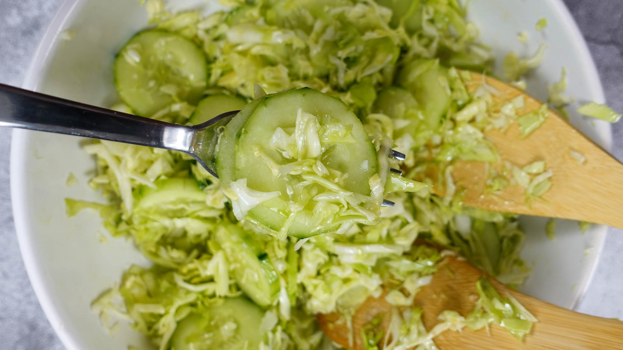 Mediterranean Cabbage Cucumber Salad in a big white bowl with a fork in one hand.