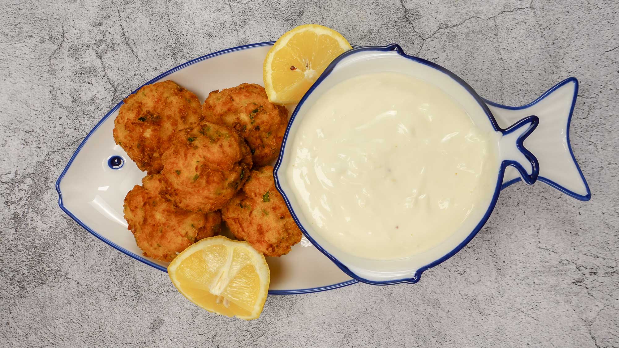 Golden shrimp croquettes served with a sauce and lemon on a dish.