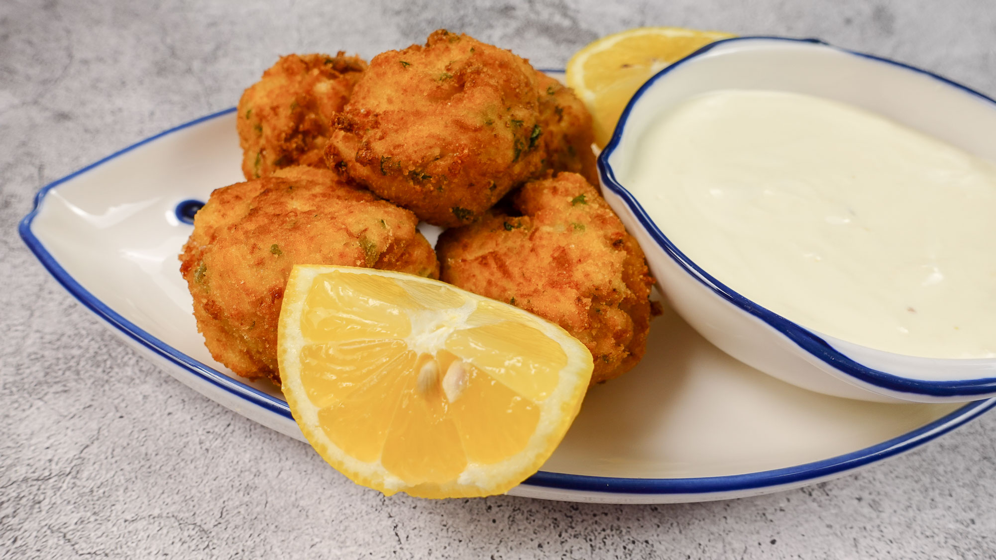 Irresistible shrimp croquettes on a plate, with pieces of lemon and a sauce in a bowl served next to them. 